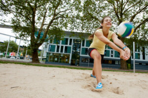 Eine Person spielt Beachvolleyball und baggert den Ball im Sand.