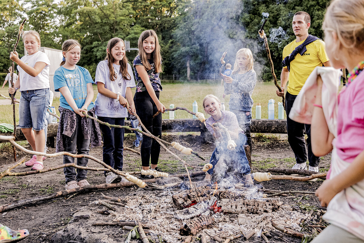 Eine Gruppe von Mädchen backt Stockbrot am Lagerfeuer