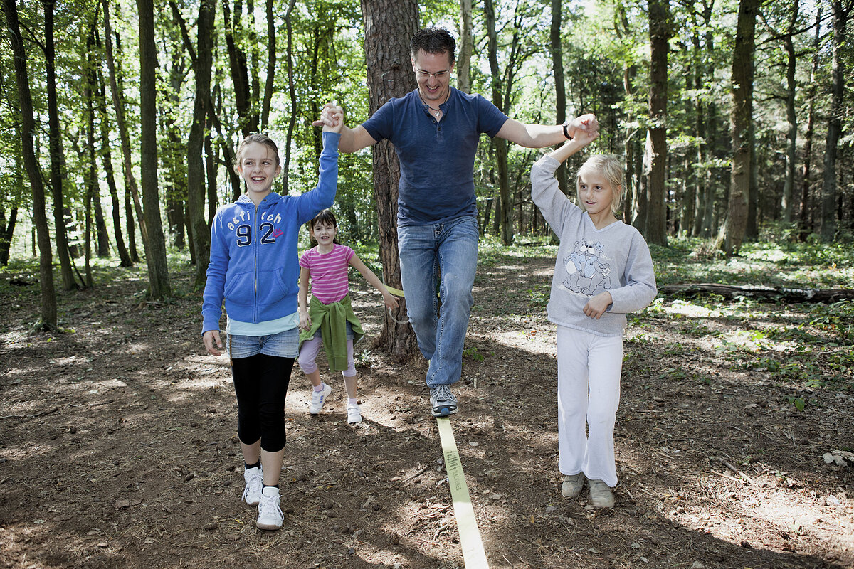 Ein Mann auf einer Slackline, links und rechts je ein Mädchen, das ihn an der Hand hält