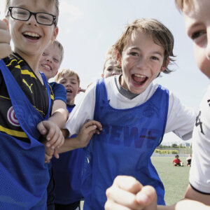 Kinder in blauen Leibchen jubeln auf dem Fußballplatz