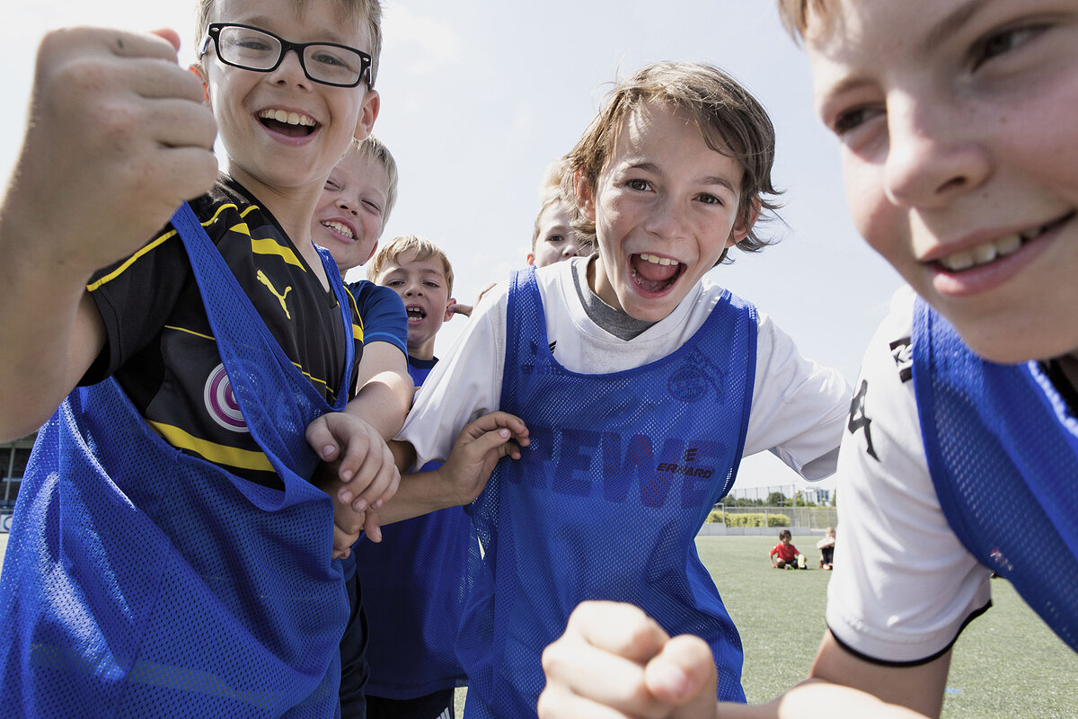 Kinder in blauen Leibchen jubeln auf dem Fußballplatz