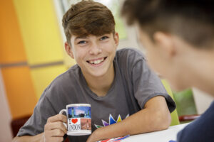 Ein lächelnder Teenager am Tisch hält eine Kaffeetasse mit London-Motiv.