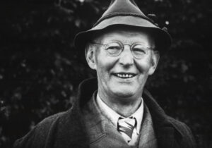 Schwarz-Weiß-Foto eines lächelnden, älteren Mannes mit Brille, Krawatte und Hut