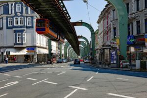 Eine orange-blaue Schwebebahn fährt über einer befahrenen Stadtstraße in Wuppertal