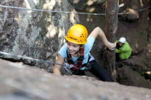 Das Bild zeigt ein Mädchen, dass mit Kletterausrüstung an einem Felsen klettert.