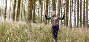 Eine Frau läuft durch hohes Gras im Wald und genießt ihre Umgebung.