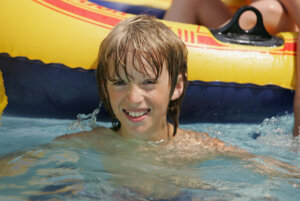 Ein Junge im Schwimmbad. Hinter ihm ein Schlauchboot
