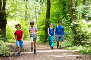 Eine Familie wandert durch einen Wald, die Kinder rennen vorweg, die Eltern gehen hinterher.