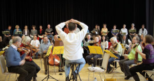 Ein Orchester beim Proben. Der Dirigigent sitzt mit dem Rücken zur Kamera.