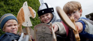 Drei kleine Jungen als Ritter verkleidet mit Holzpferd und Holzschwertern
